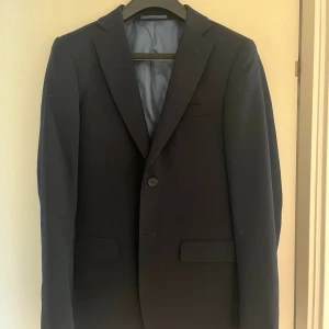 Mörkblå kostym & vit skjorta Dressmann - Hel kostym som är i mycket gott skick. Snygg mörkblå kavaj med klassisk passform och enkel knapp framtill, samt vit skjorta med krage. Passar någon som är 180cm lång. Pris kan diskuteras 