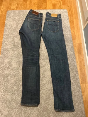 Blå jeans från Tiger of Sweden - Just nu kör jag 1 för 2 på två snygga blå jeans från Tiger of Sweden med klassisk femficksdesign och ljusbruna detaljer på bakfickan för 250kr! Mycket bra skick dessutom, missa inte! Jeansen har en rak passform och är tillverkade i mjukt denimtyg med subtil tvättad look. Perfekt för dig som gillar stilrena och tidlösa jeans.