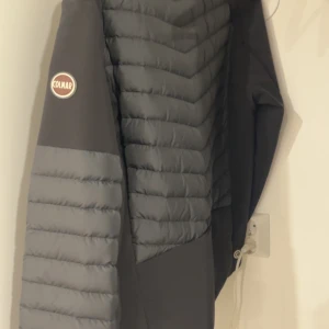 Grå pufferjacka från Colmar - Snygg grå pufferjacka från Colmar Originals med quiltad design och dragkedja. Jackan har lång ärm, en bröstficka med dragkedja och coolt märke på ärmen. Perfekt för dig som vill ha en stilren och varm jacka med modern look.