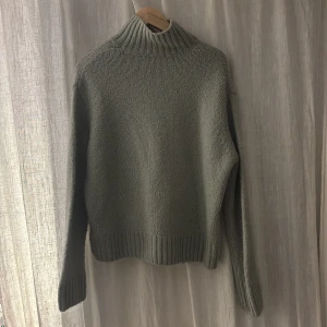 Blågrå stickad polotröja med ribbad krage - Mysig blå grå stickad polotröja med bred ribbad krage och muddar vid ärmslut och nederkant. Tröjan har en klassisk, lite loose passform och är perfekt för kyliga dagar. Enkel och stilren design som funkar till jeans eller cargo pants.