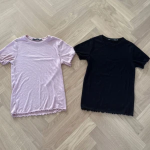 2 ribbade toppar från 157 XS - Två ribbade toppar från 157 i storlek XS, en ljusrosa och en svart. Båda har korta ärmar, rund halsringning och vågig kant nedtill. Materialet är mjukt och stretchigt, perfekt för en chill look. Säljes som ett set!