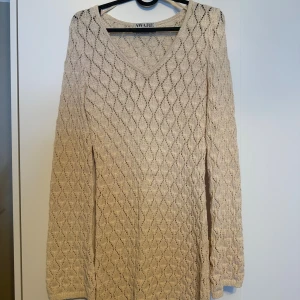 Beige stickad klänning/strandklänning från AWARE - Superfin beige stickad klänning från AWARE med v-ringad hals och långärmad design. Klänningen har ett snyggt ribbat mönster och sitter normal mot kroppen. Använd max 2 gånger. 
