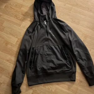 Mörkgråttt Nike Air Max Sett  - Nike mjukisbyxor i Mörk grått med snygga detaljer som dragkedjor på fickorna och ribbade muddar vid bensluten. Byxorna har en relaxed passform och är gjorda i ett mjukt syntetmaterial som känns skönt mot huden. Perfekta för chill eller träning.Både Byxorna och Hoodien för 1000kr