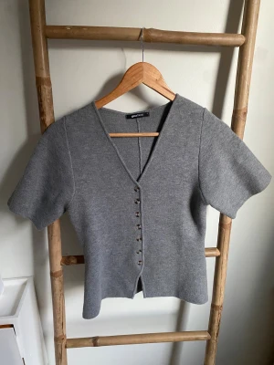 Grå stickad topp från Gina Tricot - Använd 2-3 gånger. Säljer en grå stickad topp från Gina Tricot i storlek S. Toppen har korta ärmar, v-ringning och snygga knappar framtill. Den är i en mjuk stickad kvalitet och har en normal passform som sitter skönt på kroppen.