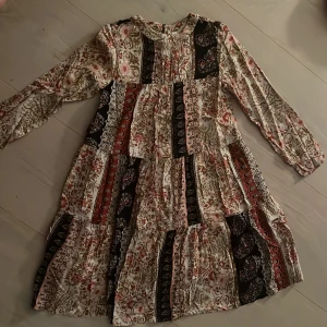 Blommig långärmad klänning från Zara - Supersöt långärmad klänning från Zara  med blommigt mönster i beige, svart, rött och rosa. Klänningen har volanger och en luftig passform, perfekt för dig som gillar boho-stil. 