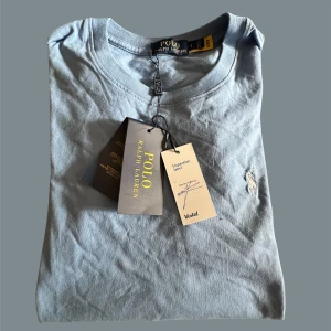 Blå t-shirt från Polo Ralph Lauren - VERIFIED FRÅN VINTED Snygg blå t-shirt från Polo Ralph Lauren med klassisk rund hals och broderad logga på bröstet. Tillverkad i mjuk bomull och har en clean, stilren look. Perfekt för dig som  ej äkta gillar enkel men exklusiv stil.