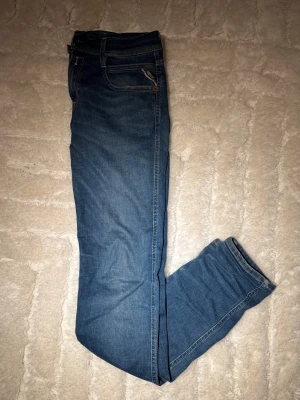 Blå Replay Anbass Hyperflex jeans - Säljer ett par blå Replay Anbass Hyperflex jeans med klassisk femficksdesign och snygga kontrastsömmar. Jeansen har lite skinny passform och är tillverkade i stretchigt denim för extra komfort. Märkespatch i skinn baktill och dragkedjegylf. De har lite slitningar men inget som syns tydligt eller förstör. 