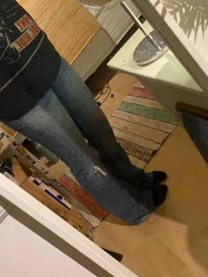Blå bootcut jeans med hål - Säljer ett par blå jeans med bootcut-snitt och slitna detaljer vid knäet.