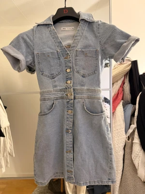 Kort jeansklänning från Zara - Säljer en  ljusblå trendig jeansklänning från Zara i storlek XS. Materialet är klassisk denim och modellen är figurnära upptill med lätt utställd kjol. Mycket bra skick!! 