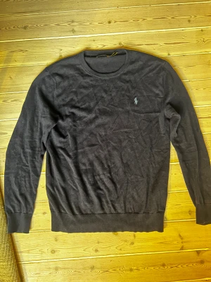 Mörkblå stickad tröja från Polo Ralph Lauren - Snygg mörkblå stickad tröja från Polo Ralph Lauren med klassisk rund hals och broderad logga på bröstet. Tröjan har långärmade ribbade muddar och är perfekt för dig som gillar stilrena och tidlösa plagg. Passar dig som vill ha en enkel men ikonisk look. Skick 9/10. Nypris: 2399kr