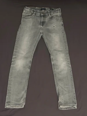 Grå jeans Scotch & Soda - Snygga grå jeans från Scotch & Soda, modell Dean. De har en skinny passform och klassisk femficksdesign. Jeansen är tillverkade i jeansmaterial och har en liten sliten detalj på framsidan för en cool look. Perfekt för dig som gillar stilrena och moderna jeans.