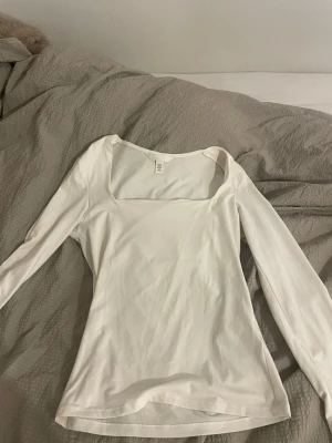 Vit långärmad topp från H&M - Säljer en stilren vit långärmad topp från H&M i storlek XS. Toppen har en fyrkantig urringning och är figurnära i modellen. Perfekt att matcha med jeans eller kjol för en enkel och snygg look.