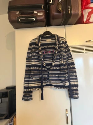 Randig kofta från Odd Molly, blå/vit - Säljer en stickad kofta från Odd Molly. Koftan har ett snyggt randigt mönster i marinblått, vitt och beige, med broderad text på insidan. Den har långa ärmar, krage och knytband framtill. Perfekt för dig som gillar avslappnad och cool stil. Storlek 2 som enligt deras storleksguide motsvarar en M. Mer använd men fint skick. Kan ha små tecken på användning. 