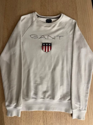 Vit Gant sweatshirt  - Vit Gant sweatshirt med stor Gant logga på bröstet, storlek XS, nypris ca 600kr. Köpt i Gant butik. Lite sliten vid ärm muddarna och loggan på bröstet men fult användbar. Tveka inte att höra av dig vid funderingar!