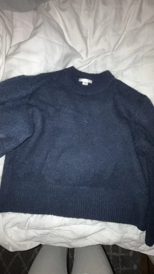 Mörkblå stickad tröja med rund hals - Mysig mörkblå stickad tröja med rund hals och ribbade muddar vid ärmslut och nederkant. Tröjan har en loose passform och är långärmad, perfekt för kyliga dagar. Enkel och stilren design som funkar till många olika outfits.I barnstorlek 142,156 men sitter som en xs.