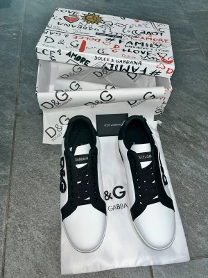 Dolce & Gabbana sneakers svart/vit - Snygga sneakers från Dolce & Gabbana i svart och vitt med coola D&G-applikationer på sidan och tydlig logga på hälen. Skorna har snörning, rund tå och platt sula. Tillverkade i skinn med svarta detaljer och vit bas. Perfekt för dig som gillar statement pieces och italiensk design.