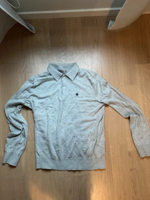 Grå pikétröja från Morris, storlek S - Snygg grå långärmad pikétröja från Morris i mjuk stickad bomull. Klassisk krage med två knappar framtill och diskret Morris-logga på bröstet. Perfekt för dig som gillar stilrena och bekväma plagg med lite preppy känsla.