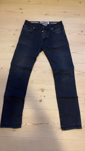 Mörkblå jeans från Jacob Cohën - Snygga mörkblå jeans från Jacob Cohën med raka ben och klassisk femficksdesign. Byxorna är tillverkade i Italien och har detaljer i guld på knapparna samt en patch med logga. Bra skick, sliten patch där bak. Hör av dig vid frågor🤗🤗