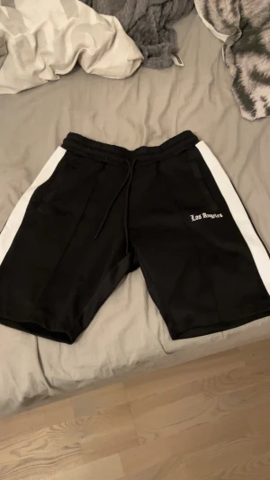 Los angels shorts - Svarta los angels shorts i storlek XS med vita sidopaneler och snörning i midjan. Trycket 'Los Angeles' på ena benet ger en cool vibe. Perfekta för chill eller sportiga dagar, med normal passform och mjukt syntetmaterial.