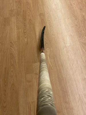 Svart innebandyklubba från Zone - Säljer en stilren innebandyklubba från oxdog med svart blad och svart skaft med röda detaljer. Greppet är lindat med ljusbeige tejp och har ett mönster av vita snören för extra grepp. Perfekt för dig som vill ha kontroll och snygg design på planen.