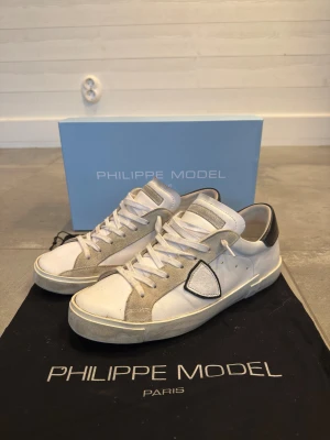 Vita Philippe Model skor - Säljer mina vita Philippe Model skor med svart häl. De är köpta ifrån merchsweden.se för 3200 kr (kvitto finns). Skorna är i storlek 42 och är i ett mycket bra skick (8/10), förutom att sulorna där bak är lite slitna. Box och dustbag ingår, inklusive kvitto. Skriv för fler bilder eller ifall du har några generella funderingarna!