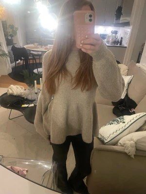 Stickad tjocktröja, utsvängd  - En beige stickad tjocktröja som är utsvängd vid magen.