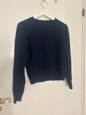 Mörkblå stickad tröja från Lindex - Mörkblå stickad tröja från Lindex med rund hals och ribbade muddar vid ärmslut och nederkant. Klassisk och enkel design som funkar till många olika stilar. Perfekt för dig som gillar mjuka och sköna tröjor med lång ärm.