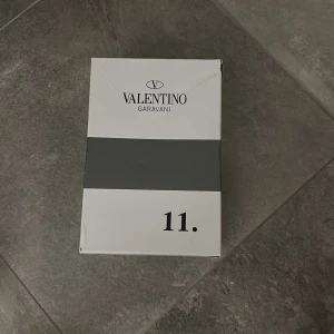 Valentino Garavani Open sneakers vit/svart - Säljer ett par Valentino Garavani Open sneakers i vitt skinn med bred svart läderdetalj över mitten. Klassisk rund tå, snörning och platt sula. Märkeslogga på plösen och boxen medföljer. Perfekta för dig som gillar lyxiga och stilrena sneakers.