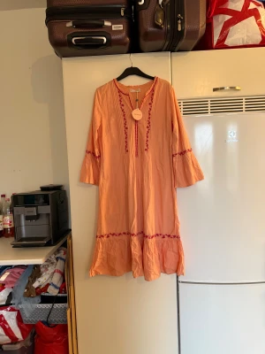 Peachfärgad Dolores Dress Odd Molly - Superfin peachfärgad klänning från Odd Molly, modell Dolores Dress. Långklänning med trekvartsärm, broderade detaljer i mörkrosa och volang nertill. Luftig och lätt i bomull, perfekt för varmare dagar. Säljs med originaltagg kvar. Från märket Odd Molly. Storlek 2 som enligt deras storleksguide motsvarar en M. Helt ny med tags/ prislapp fortfarande kvar. 