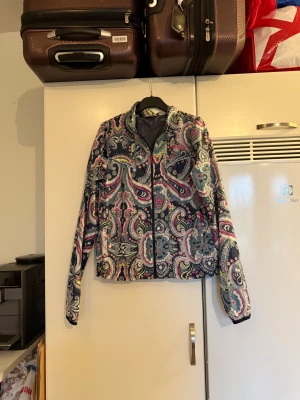 Mönstrad vindjacka Odd Molly - Färgglad vindjacka från Odd Molly med paisleymönster i blått, rosa, gult och vitt. Jackan har dragkedja framtill, hög krage och elastisk nederkant. Lätt och smidig med meshfoder på insidan, perfekt för dig som vill sticka ut. Från märket Odd Molly. Storlek 2 som enligt deras storleksguide motsvarar en M. Mycket fint skick, jag hittar inga synliga anmärkningar eller defekter. 
