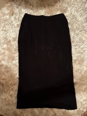 Svart stickad långkjol från Gina Tricot - Svart långkjol från Gina Tricot i stickat material med snyggt hålmönster. Kjolen har rak passform och är midilång, perfekt för dig som gillar en enkel men cool look. Materialet är mjukt och följsamt, vilket gör den bekväm att bära hela dagen.