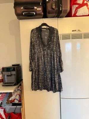 Mörkgrå blommig kortklänning - Supersöt mörkgrå kortklänning med blommigt mönster och v-ringad hals med volangkant. Klänningen har långa ärmar och ett flowy, avslappnat fall. Materialet känns lätt och luftigt, perfekt för dig som gillar boho-vibe och detaljer som sticker ut. Från märket Odd Molly. Storlek 2 som enligt deras storleksguide motsvarar en M. Mycket fint skick, jag hittar inga synliga anmärkningar eller defekter.  