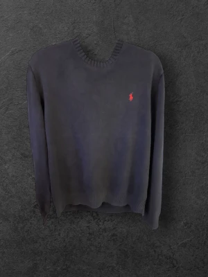 Mörkblå stickad tröja Polo Ralph Lauren - Snygg mörkblå stickad tröja från Polo Ralph Lauren i storlek L. Tröjan har rundad hals, ribbade muddar och den klassiska röda Polo-loggan broderad på bröstet. Perfekt för dig som gillar stilrena och tidlösa plagg med premiumkänsla.