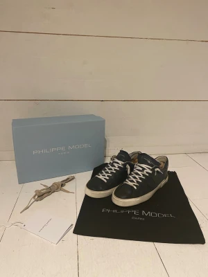 Philippe Model mörkblå  - Snygga mörkblå sneakers från Philippe Model i äkta läder med vita sulor och vita skosnören. Klassisk låg modell med diskret logga på sidan. Kommer med originalkartong, orginal skosnören och dustbag. Är en defekt i hällen men syns inte eller påverkas vid användning. Pris kan diskuteras.
