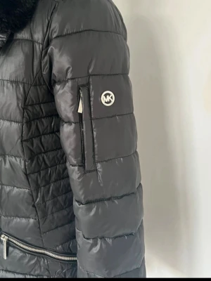 Svart jacka från Michael Kors!  - Snygg svart jacka från Michael Kors med hög krage och två dragkedjeförsedda fickor framtill. Jackan har quiltad design, diskret logga på ärmen och dragkedja i silver. Perfekt för kalla vinterdagar och riktigt stilren look. Knappt använd! 🤗finns pälskrage till som man sätter på kragen om man vill. Och luva. 