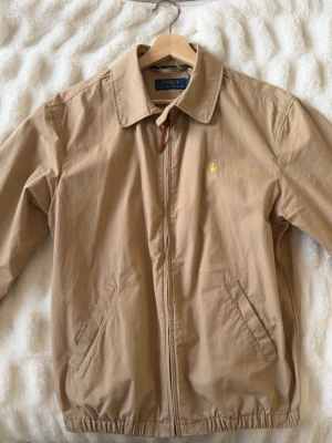 Polo Ralph Lauren Bayport jacka – S - Säljer en klassisk Polo Ralph Lauren Bayport-jacka i khaki/beige. Tidlös modell som passar till allt. 	•	Storlek: S 	•	100 % bomull 	•	Dragkedja 	•	Broderad logga 	•	Mycket fint skick  Nypris ca 2 000–2 500 kr. 💰                         Pris: 1 100 kr Betalning via Plick.