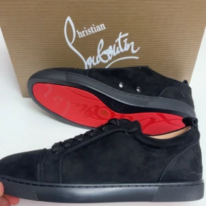 Christian Louboutin svarta sneakers - Svarta sneakers från Christian Louboutin med klassisk röd sula och broderad logga på hälen. Skorna har rund tå, snörning och platt sula. Materialet är mocka och detaljerna är stilrena och lyxiga, perfekt för dig som gillar exklusiv streetstyle.