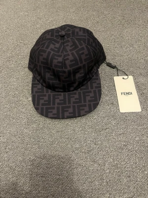 Svart keps med Fendi-logga - Snygg svart keps från Fendi med det klassiska FF-monogrammet över hela kepsen. Kepsen har böjd skärm och justerbar baksida. Tillverkad i ett slitstarkt tygmaterial och levereras med originaltagg.