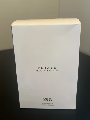 Zara Petale Santale Eau de Parfum - Zara Petale Santale Eau de Parfum i en stilren vit kartong. Parfymen kommer i en 100 ml förpackning och har en minimalistisk design med svart text. Perfekt för dig som gillar eleganta och enkla dofter.