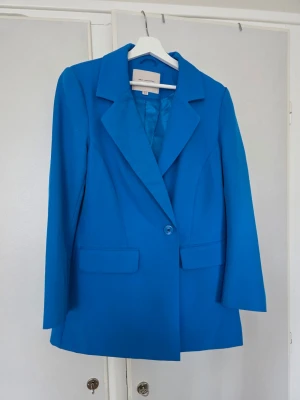 Blå kavaj från Only Carmakoma strl 42 - Snygg blå kavaj från Only Carmakoma med klassisk krage, en knapp framtill och två fickor med lock. Fodrad insida med diskret prickmönster. Perfekt för att lyfta din outfit med en färgklick.