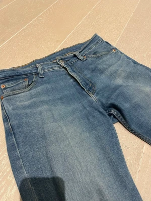 Blå raka jeans med klassisk passform - Säljer ett par blå jeans i klassisk rak modell med fem fickor och bälteshällor. Jeansen har en lätt tvättad look och är tillverkade i denim. Perfekta för en avslappnad stil och passar till det mesta.