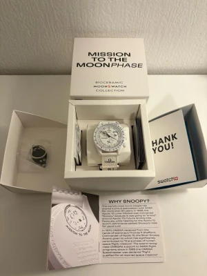 Swatch x Omega MoonSwatch vit klocka - Säljer en Swatch x Omega MoonSwatch Mission to the Moonphase 'Snoopy' i vit biokeramik. Klockan har en rund urtavla med svarta detaljer och Snoopy-motiv, samt vit rem. Skriv för mer information