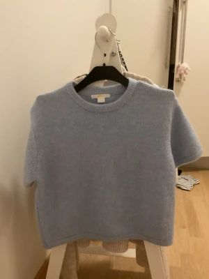 Ljusblå stickad tröja Gina Tricot young - Mysig ljusblå stickad tröja från Gina Tricot med korta ärmar och rund hals. Perfekt för att addera lite färg till din garderob. Tröjan har en enkel och clean look som funkar till många olika stilar.