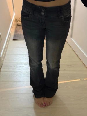 Svarta bootcut jeans med låg midja från Bershka - Snygga svarta bootcut jeans med låg midja och klassiska fem fickor. Jeansen har en lätt tvättad look och stängs med dubbla knappar och dragkedja. Storlek 32