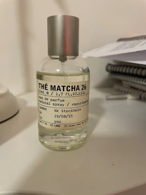 Le Labo Thé Matcha 26 parfym 50ml - Le Labo Thé Matcha 26 är en exklusiv parfym i en stilren, genomskinlig glasflaska med silverfärgad metallkork. Flaskan rymmer 50 ml och har en minimalistisk etikett med svart text. Doften är inspirerad av matcha-te och har en modern, fräsch känsla. Den är köpt från NK, kvitto finns. Frakt tillkommer 