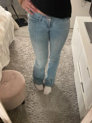 Ljusblå bootcut jeans med brodyr - Säljer ett par ljusblå bootcut jeans med snygg broderad detalj i rosa på bakfickorna. Jeansen har klassisk femficksdesign och är tillverkade i mjuk denim. Perfekta för en avslappnad och trendig look. Säljer pga att de inte är min stil 