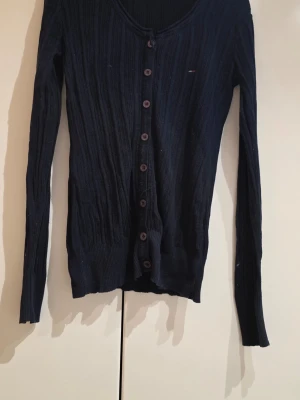 Svart ribbad kofta med knappar - Svart ribbstickad kofta med långa ärmar och knäppning framtill. Snygg och enkel modell som passar till mycket. Liten logga på bröstet.