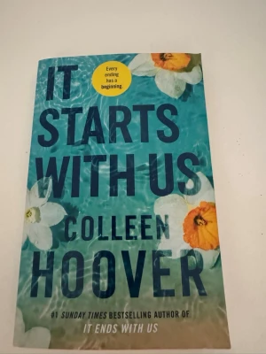 It Starts With Us av Colleen Hoover - En skönlitterär bok med blått omslag och blommotiv, skriven av Colleen Hoover. Boken är på engelska och är en uppföljare till 'It Ends With Us'. Perfekt för dig som gillar romantik och drama.