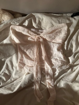 Ljusrosa spetsblus med rosett - Supersöt ljusrosa tubtopp i spets med stor rosett framtill. Blusen är axelbandslös och har en croppad passform som ger en trendig vibe. Perfekt för dig som vill sticka ut med en romantisk och feminin look. Heeelt perfekt för sommaren!