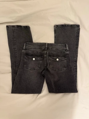 Svarta Low waist Bootcut jeans med dubbla knappar - Snygga svarta bootcut jeans med dubbla silverknappar i midjan och klassiska fem fickor. Jeansen har en tvättad look.  Materialet är stretchigt och bekvämt.